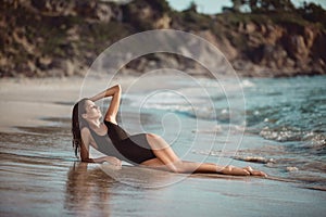 young woman in black swimsuit lying on the beach.