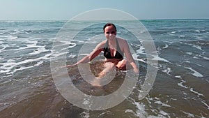 Young woman in black swimsuit spends time in sea. Adult lady swims towards the waves.