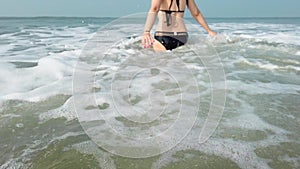 Young woman in black swimsuit spends time in sea. Adult lady swims towards the waves.