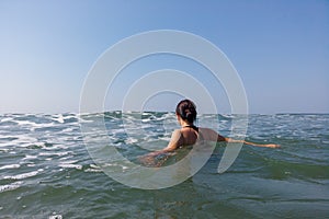 Young woman in black swimsuit spends time in sea. Adult lady swims towards the waves.