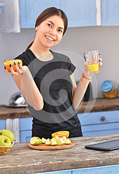 A young woman in a black t-shirt makes fit breakfast and drinks orange juice . Fruit in a bowl stands nearby