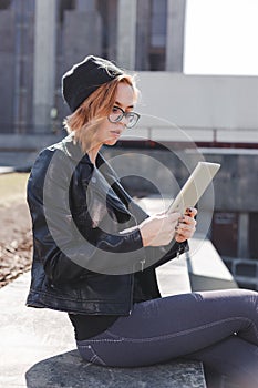 A young woman in black is using a tablet outdoor in the city.