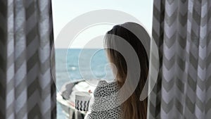 Young woman in a blanket and with a cup of coffee on the background of curtains and the sea. woman having breakfast