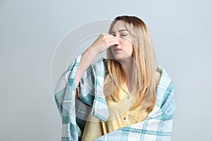 Young woman with blanket suffering from runny nose on light background