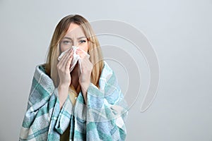 Young woman with blanket suffering from runny nose on light background. Space for text