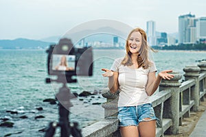 A young woman blogger leads her video blog in front of a camera by the sea. Blogger concept