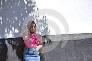 Young woman, blonde, green eyes, wearing pink t-shirt and denim skirt, looking at the ground, distracted and dreamy, leaning