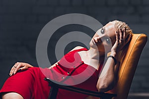 Young woman with blonde hair and a short haircut in a red evening dress lies on the chair.