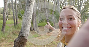 Young woman with blonde hair smiles at the camera, extending her arm towards the trees with copy spa