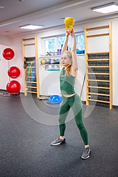 Young woman with blonde hair squatting with kettlebells in gym