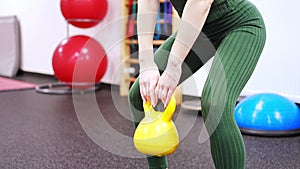 Young woman with blonde hair squatting with kettlebells in gym