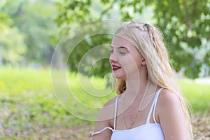 Young woman blonde long hair looking away while sitting alone in the park. Beauty cute teenager relaxed at outdoor in
