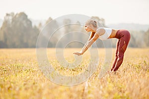 Young woman blonde in red pants and white T-shirt performs warm before running in park