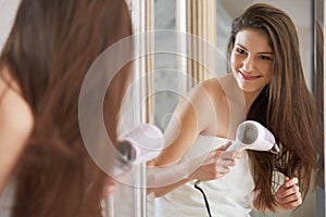 Young woman blow drying hair in bathroom