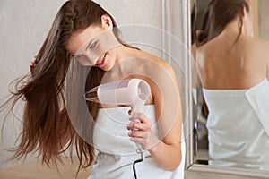 Young woman blow drying hair in bathroom