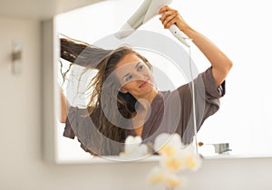 Young woman blow drying hair in bathroom