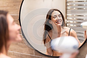 Young woman blow drying her hair in front of the mirror in the bathroom