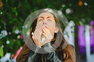 Young woman blowing her nose affected by spring allergy to pollen in a garden, with sinus problems