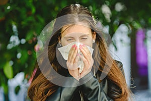 Young woman blowing her nose affected by spring allergy to pollen in a garden, with sinus problems