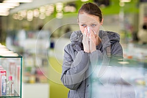 Young woman blowing her nose while in a modern pharmacy