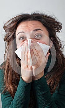 Young woman blowing her nose with paper tissue.