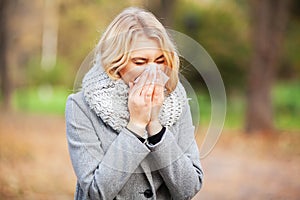 Young woman blowing her nose on the park. Woman portrait outdoor sneezing because cold and flu