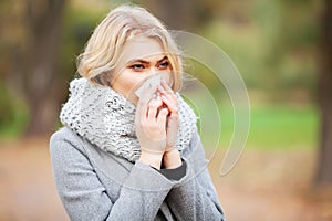 Young woman blowing her nose on the park. Woman portrait outdoor sneezing because cold and flu