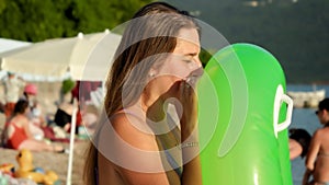 Young woman blowing inflatable swimming ring while standing on beach at sunset. Concept of tourism, happy summertime