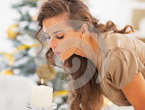 Young woman blowing out candle in front of christmas tree