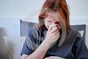 Young woman blows her nose in a napkin lying on the bed, close-up