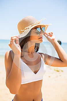 Young woman in blue bikini wearing white straw hat enjoying summer vacation at beach. Portrait of beautiful latin woman relaxing a