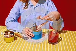 Young woman in blue blouse with doll parts on meat can, drinking tomato juice against red background