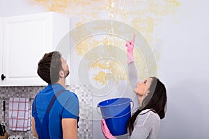 Woman Holding Bucket Showing Water Leaking From Damage Ceiling photo