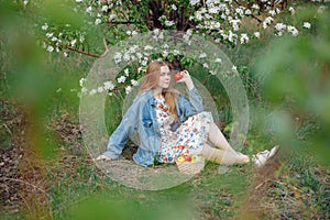 A young woman in a blue denim jacket sits in a clearing.