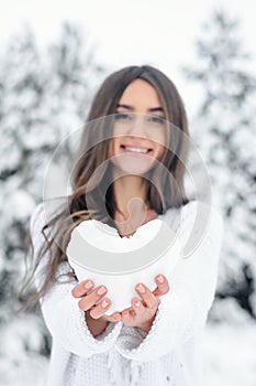A young woman in a blue dress is holding a heart from the snow i