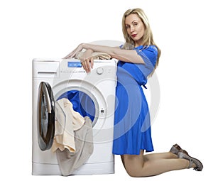 Young woman in a blue dress kneeling unloads laundry from a new washing machine