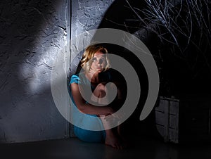 Young woman in blue dress sitting in dark horrible place