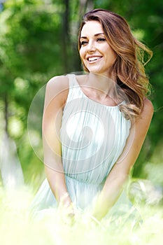 Young woman in blue dress sitting on grass