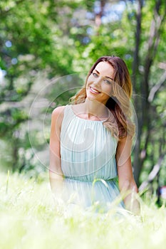 Young woman in blue dress sitting on grass