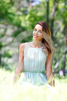 Young woman in blue dress sitting on grass