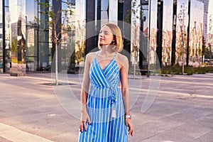 Young woman in blue dress walking alone outdoor in a park, dreams, calm face with smile.