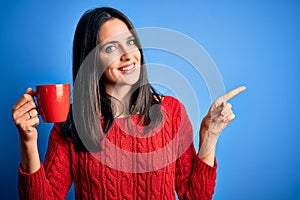 Young woman with blue eyes drinking cup of coffee standing over isolated background very happy pointing with hand and finger to