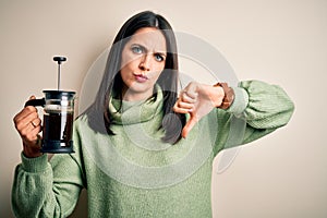 Young woman with blue eyes making cafe using coffe maker standing over white background with angry face, negative sign showing