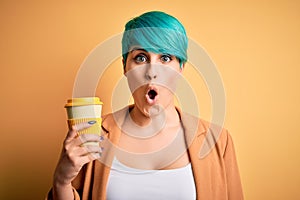 Young woman with blue fashion hair drinking a cup of coffee over yellow isolated background scared in shock with a surprise face,