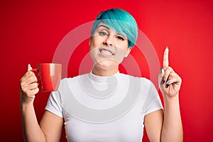 Young woman with blue fashion hair drinking a cup of coffee s over red isolated background surprised with an idea or question