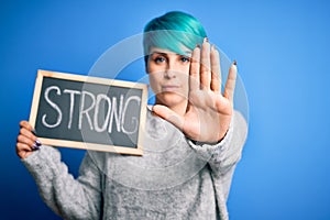 Young woman with blue fashion hair holding blackboard with strong message with open hand doing stop sign with serious and