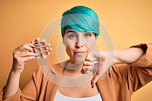 Young woman with blue fashion hair holding delicious wffle over yellow background with angry face, negative sign showing dislike