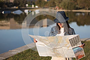 Young woman with blue hat and denim jacket consulting a map during a trip