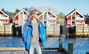Young woman in a blue jacket on a background of traditional red Norwegian Rorbu houses traveling to Lofoten Norway