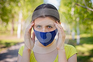 A young woman in a blue mask holds her head in her hands.